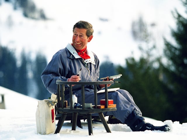 mittelalter Mann sitzt im Schnee, hält Pinsel, lacht und schaut nach rechts.