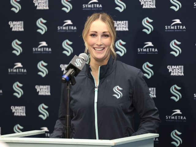 Lächelnde Frau bei einer Pressekonferenz in einer Arena.