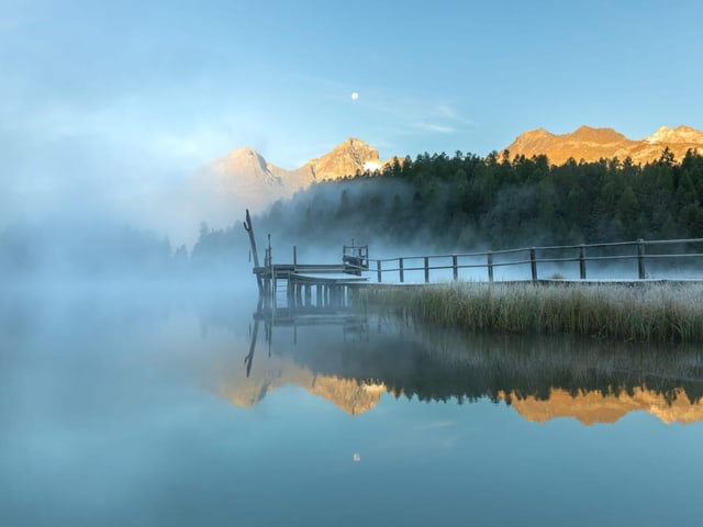 Erst die Bergspitzen werden von der aufgehenden Sonne beschienen. Der Nebel hat den Stazersee noch verzaubert.