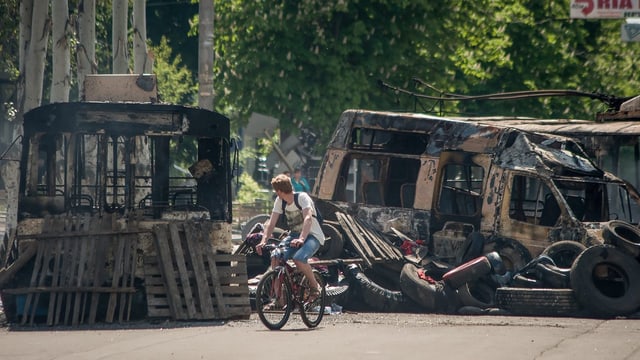 Ein Radfahrer fährt an zwei ausgebrannten Kleinwagen vorbei.