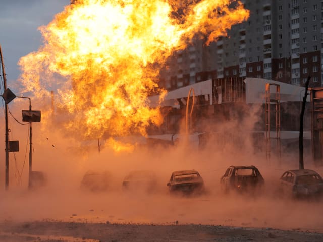 In der Dämmerung steigen Flammen aus einem Gebäude auf. Davor stehen Autors.