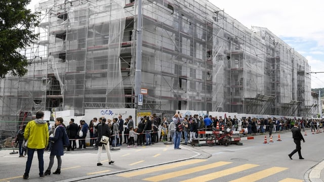 Lange Menschenschlange vor Neubaugebäude.