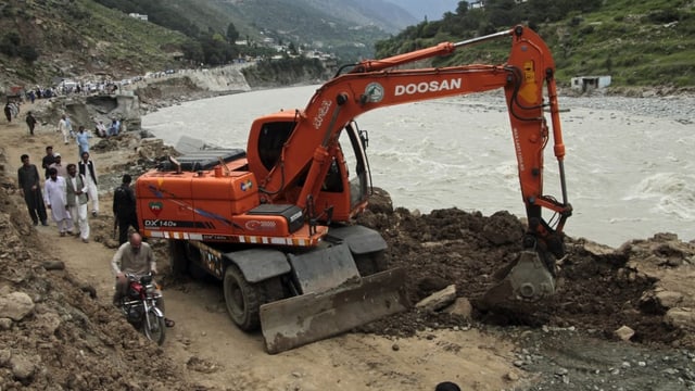 Ein Bagger in Pakistan schaufelt Steine neben einem Fluss.