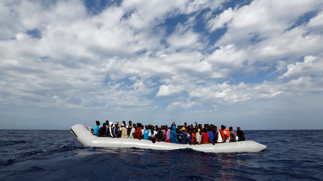 Symbolbild: Ein riesiges Gummiboot, vollgepfercht mit Menschen, dümpelt auf dem offenen Meer.