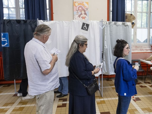 Menschen stehen in einer Schlange vor Wahlkabinen.