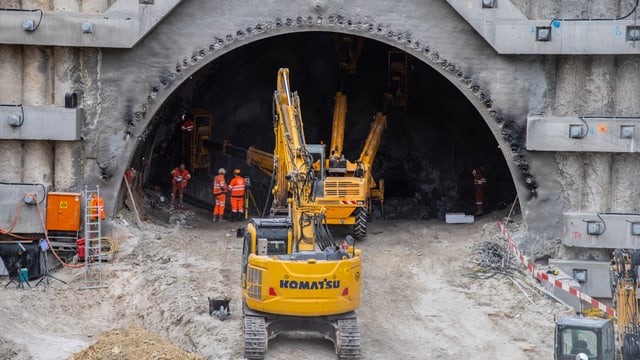 Baumaschinen vor einem Tunneleingang und einige Arbeiter