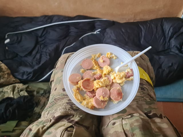 Teller mit Wurst und Rührei auf den Oberschenkeln eines Soldaten.