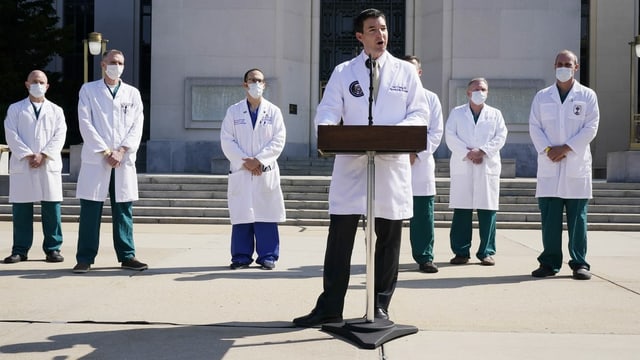 Doctor at the lectern.  Behind them more doctors.