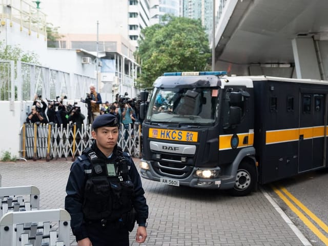 Ein Polizist steht hinter einer Absperrung, ein kleines Lastwagen fährt hinter ihm vorbei.