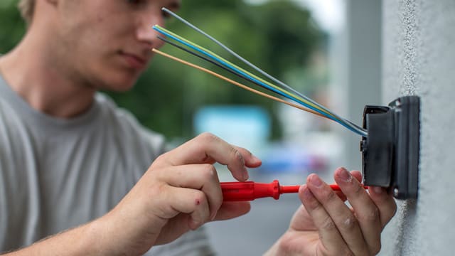 Zwei Hände mit einem Schraubenzieher montieren eine Steckdose