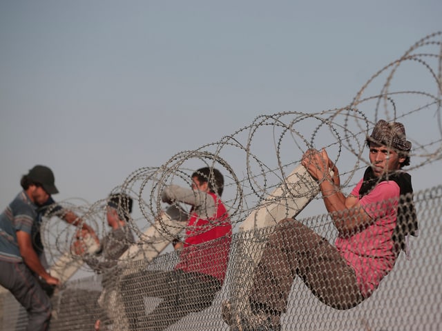 Syrische Männer klettern den Stacheldraht hoch.