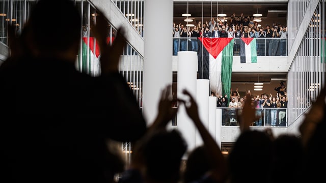 Menschen winken palästinensischer Flagge in modernem Gebäude zu.