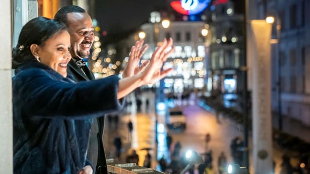 Abiy und seiner Frau winken bei Nacht von einem Balkon.