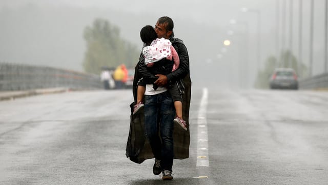 Ein Mann trägt im strömenden Regen sein Kind auf den Armen