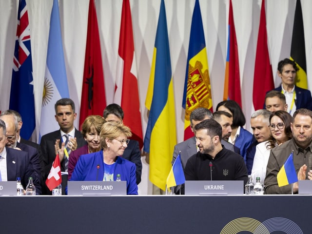 Menschen bei einer Konferenz mit Länderflaggen im Hintergrund.