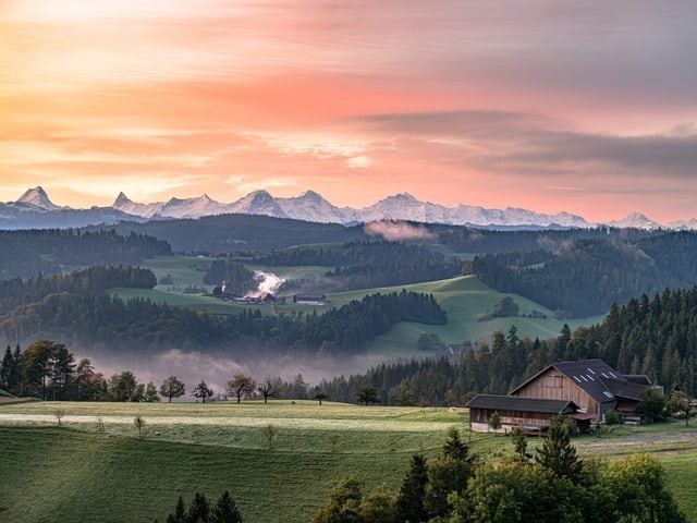 Alpenpanorama bei Sonnenaufgang mit Bauernhof im Vordergrund.