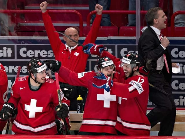 Jubelnde Eishockeyspieler und Trainer in roten Trikots an der Bande.