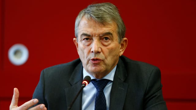 Wolfgang Niersbach in einem Anzug vor einem roten Hintergrund