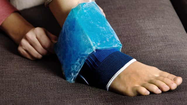 Verstauchter Fuss mit Bandage und Kühlmanschette auf Sofa.