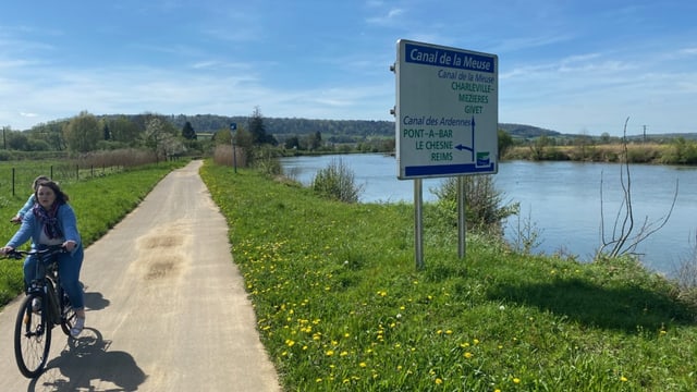 Eine Frau fährt Fahrrad auf einem Weg neben dem Canal de la Meuse.