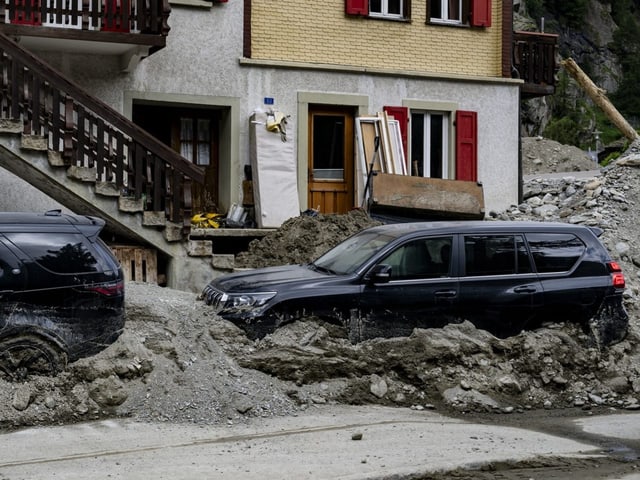 Autos in Schlamm vor einem Haus nach einem Erdrutsch.