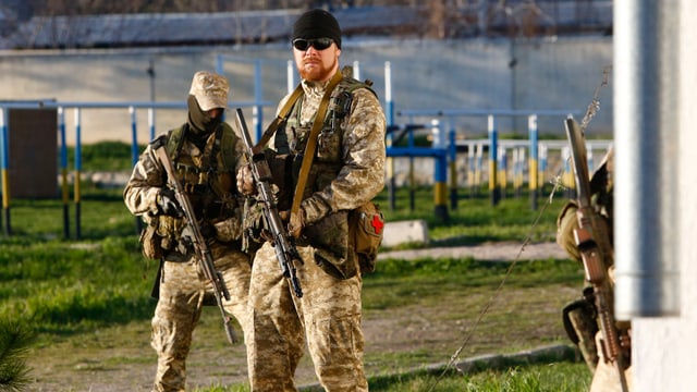 Drei schwer bewaffente Soldaten mit Gesichtsschutz oder Sonnenbrillen.