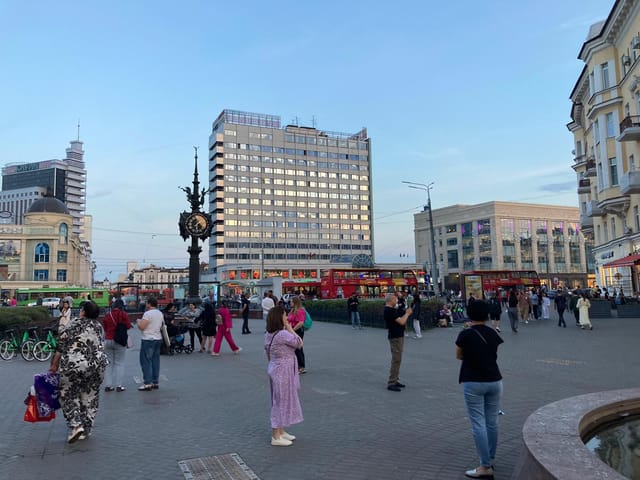 Stadtplatz mit Menschen und Hochhäusern im Hintergrund am Abend.