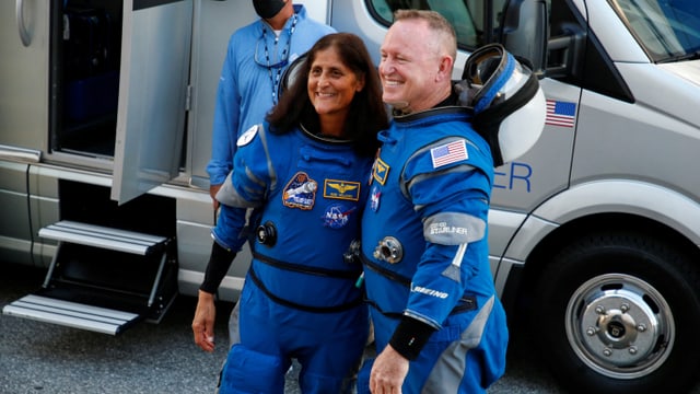 Zwei Astronauten in blauen Anzügen vor einem Fahrzeug.