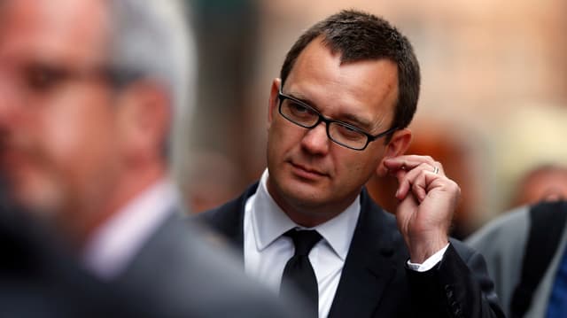 Andy Coulson, im Anzug, kratzt sich am linken Ohrläppchen.