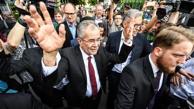 Van der Bellen inmitten von Personen, er hat die Arme erhoben.