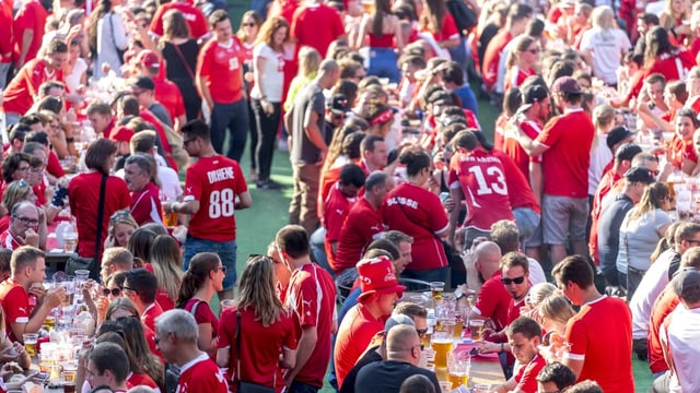 Menschen in Schweiz-Trikots sitzen am Public Viewing an langen Tischreihen und trinken Bier.