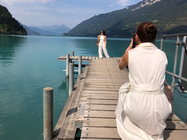 Eine weissgekleidete Frau fotografiert eine zweite weissgekleidete Frau, die am Ende eines Stegs steht