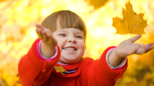 Ein kleines Mädchen wirft Herbstblätter in die Luft