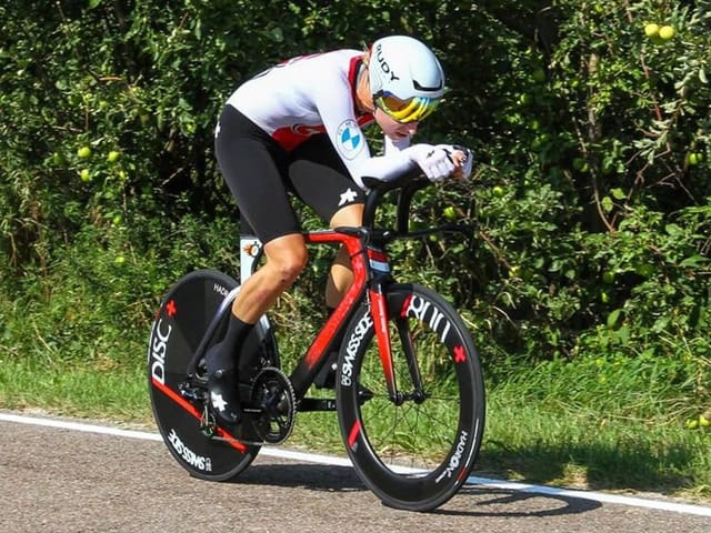 Radrennfahrer in Aeroposition fährt auf einer Strasse.