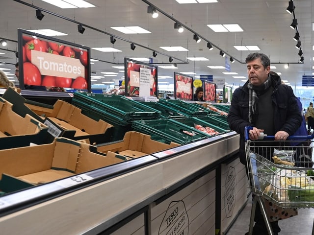 Ein Mann schiebt einen Einkaufswagen an einer leeren Auslage vorbei, wo eigentlich Tomaten sein sollten.