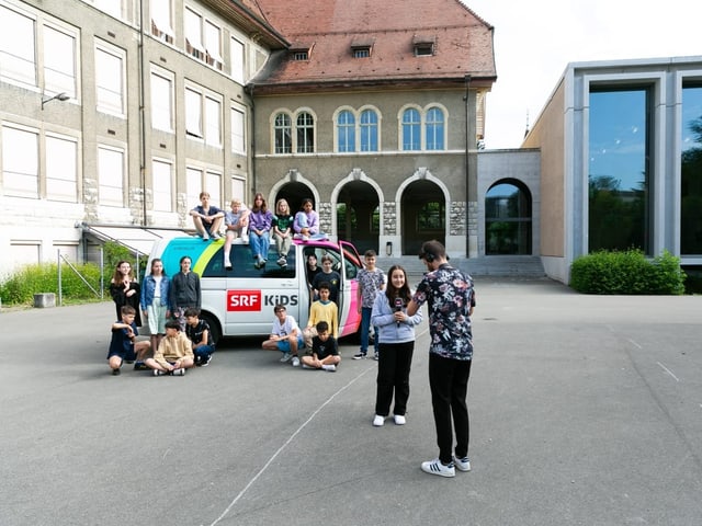 Eine Schülerin hält ein Mikrofon in der Hand, der Rest der Klasse steht hinter ihr.