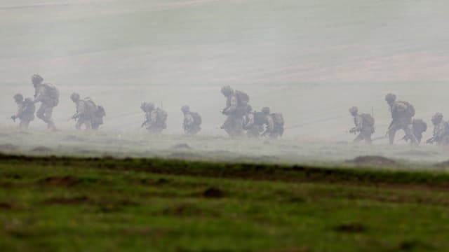 Nato-Manöver in Rumänien: Vollbepackte und bewaffnete Soldaten rennen über ein Feld, fotografiert aus grosser Entfernung.