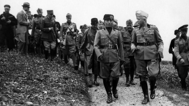 Schwarzeweissfoto: Mussolini geht neben General Badoglio einer Soldatentruppe voran.