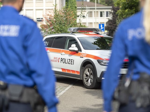 Eine Polizistin und ein Polizist von hinten, unscharf. Zwischen ihnen sieht man ein Polizeiauto.