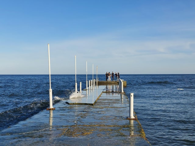 Eine Anlegestelle, die ins Meer führt, mit einigen Leuten