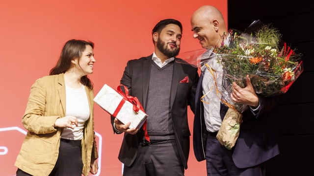 Frau und zwei Männer, einer davon mit Blumenstrauss.