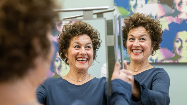 eine Frau mit kurzen Locken hält einen Spiegel hoch