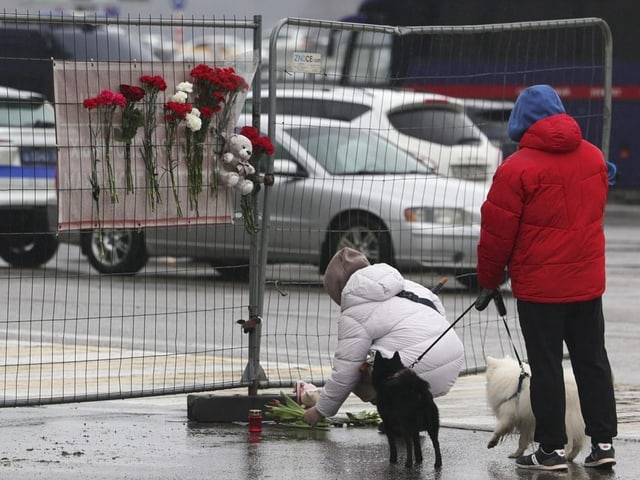 Eine Person legt Blumen vor einem Zaun nieder