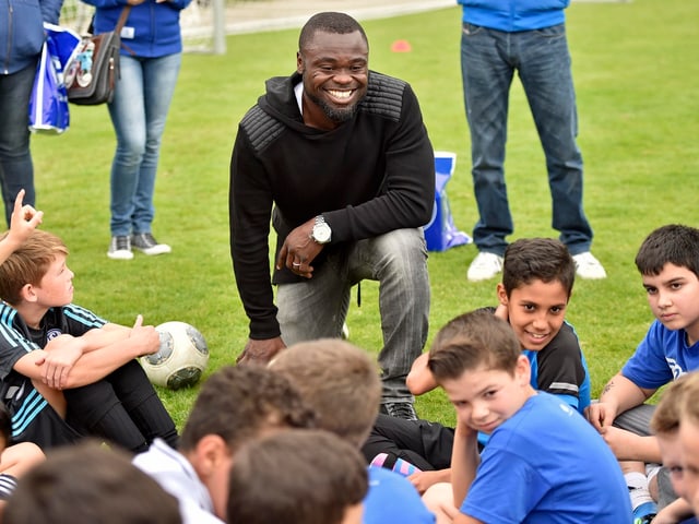 Asamoah kniet sich lachend vor einer Schar Kinder.