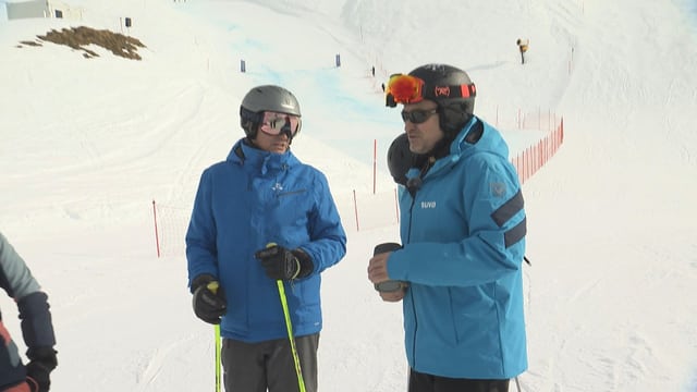 Menschen stehen auf einer Skipiste. 