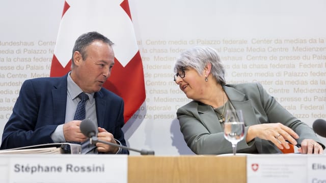 Rossini und Baume-Schneider im Medienzentrum des Bundes mit Schweizer Flagge im Hintergrund.