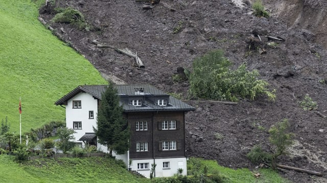 Blick auf Geröllmasse gleich neben einem Haus am Hang in Schwanden