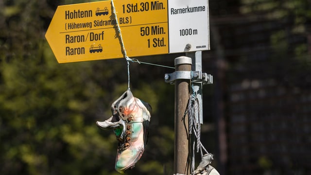 Alte Wanderschuhe hängen an einem gelben Wanderwegweiser