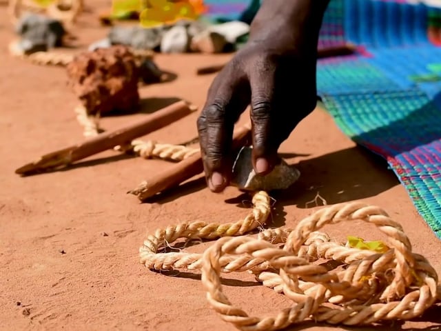 Hand arrangiert Seil und Gegenstände auf Teppich und Erde.