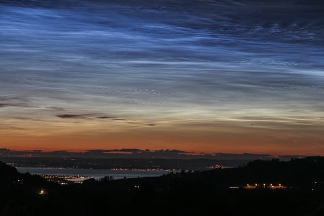 Silbern leuchtende Nachtwolken am dunklen Himmel.